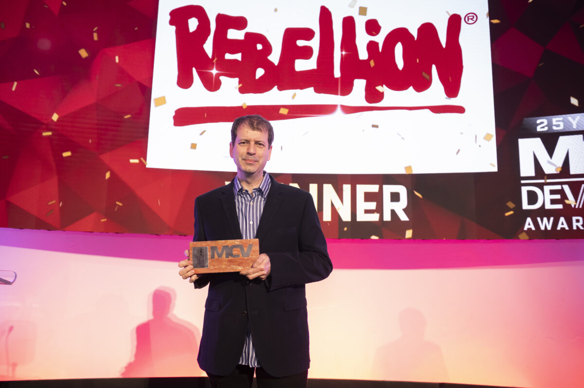 Co-founder Chris Kinglsey, OBE holds an award on stage. Behind him the Rebellion logo and the text 'winner' are projected onto the screen.
