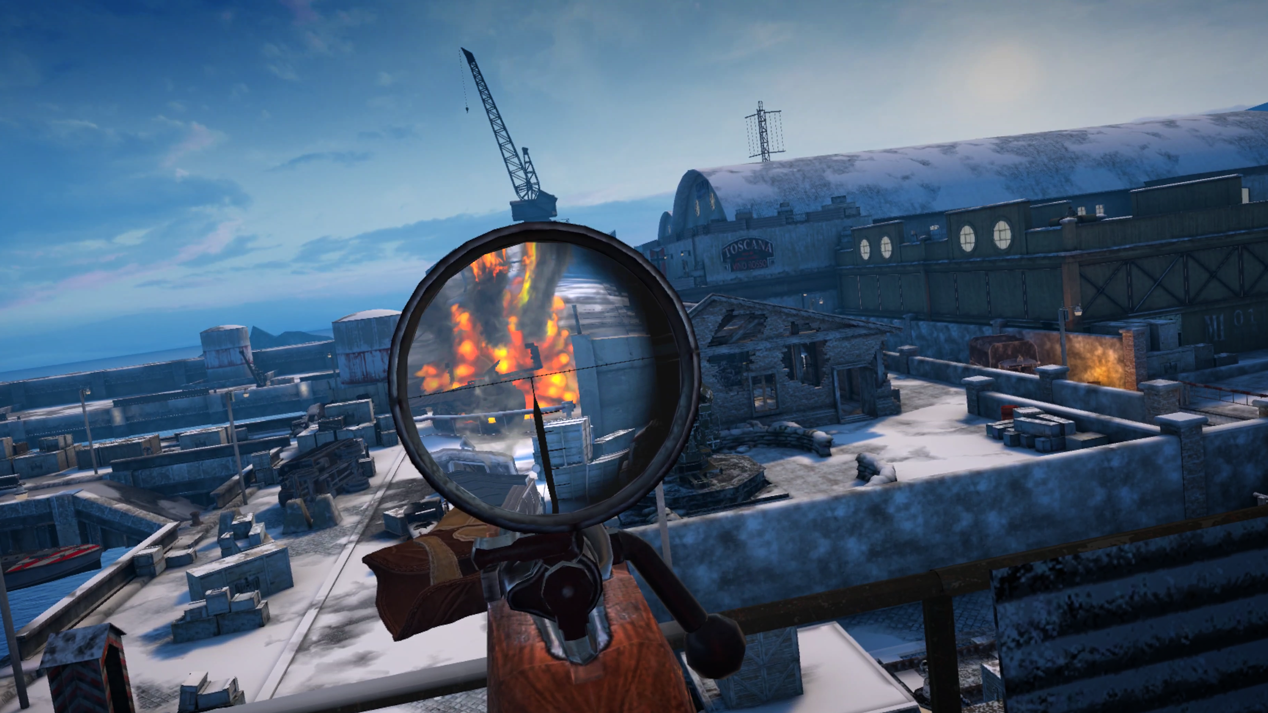 Gameplay screenshot of Sniper Elite VR Winter Warrior showing an industrial dockyard map on a sunny day. There is a first-person view of a sniper rifle which is currently scoped into the explosive aftermath of a shot.