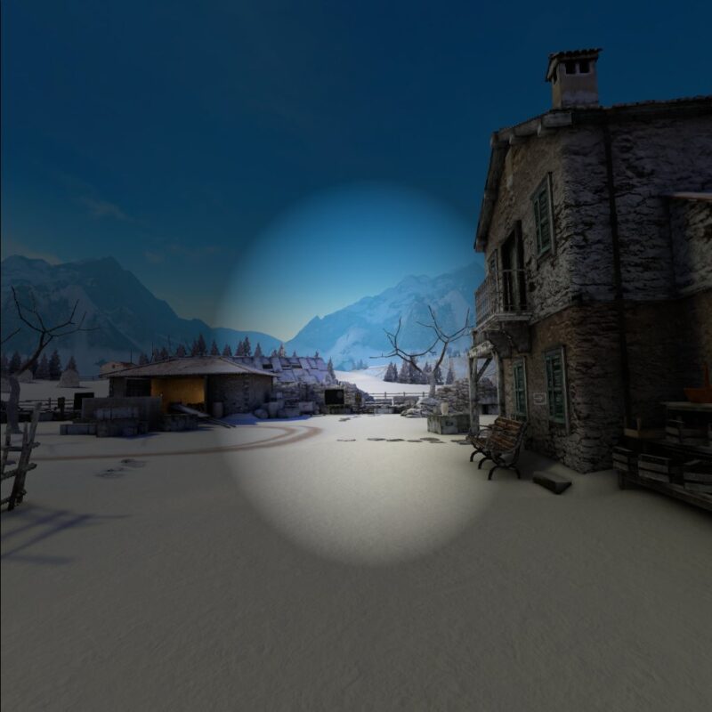 Gameplay of Winter Warrior with a vignette overlayed, which casts a semi-transparent darkness to the edges of the screen. Almost all of the scene is affected, showing a snowy courtyard with two distressed buildings, one to the right and one ahead. There are also leafless trees and many crates around the edges of the courtyard. In the distance coniferous trees can be seen, and beyond them large snowy mountains.