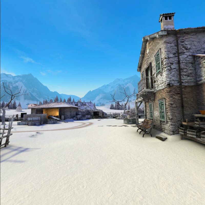 Gameplay of Winter Warrior showing a snowy courtyard with two distressed buildings, one to the right and one ahead. There are also leafless trees and many crates around the edges of the courtyard. In the distance coniferous trees can be seen, and beyond them large snowy mountains.