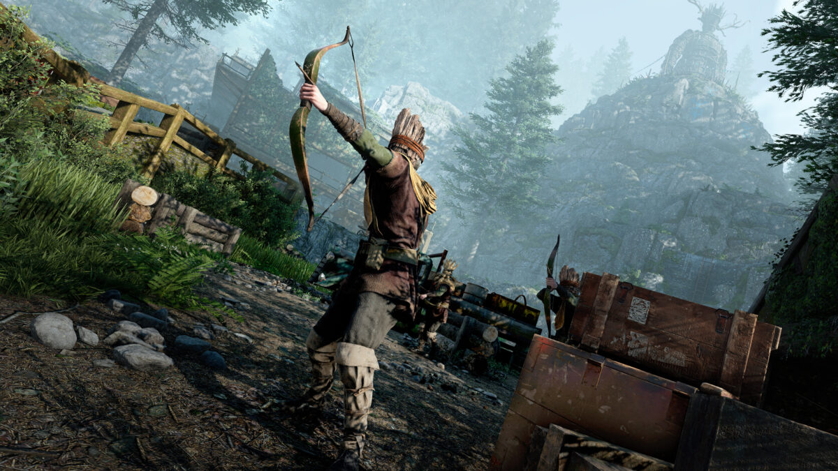 A screenshot from Atomfall showing a cult member wearing a mask with a bow and arrow aiming it towards something. Surrounded in the Woods the Wicker Man stands tall on a hill above just off in the distance.